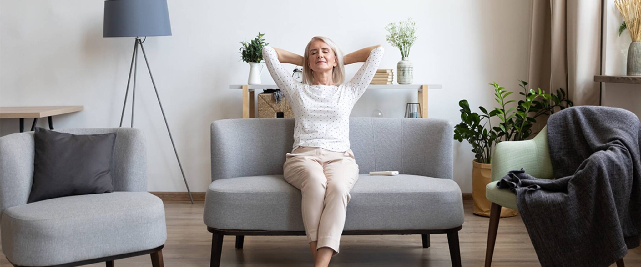 A senior woman puts her hands behind her head as she stretches and relaxes on her couch