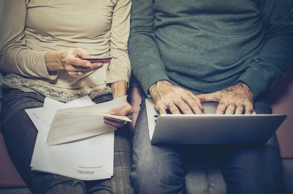 Close up of a senior man and woman's hands while working on finances on a laptop.