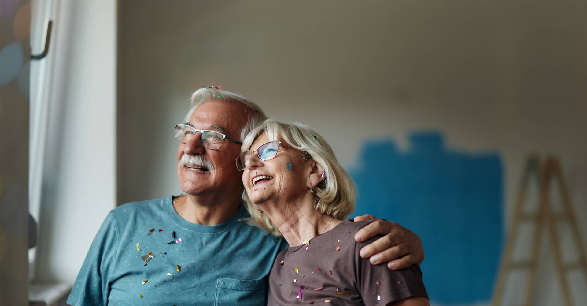 two older adults side hugging as they admire their painting