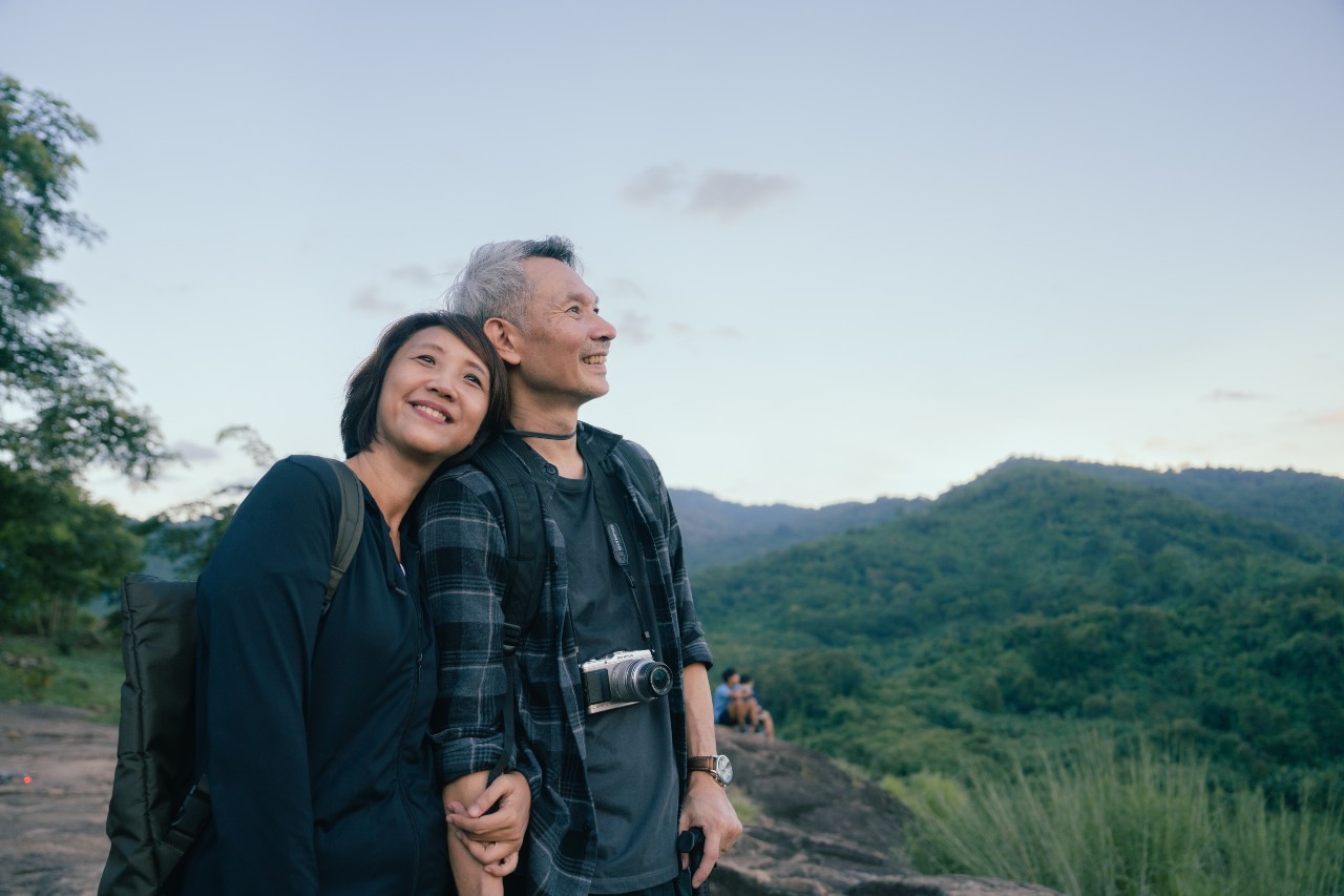 A mature man and mature woman lean against each other after taking a hike in nature