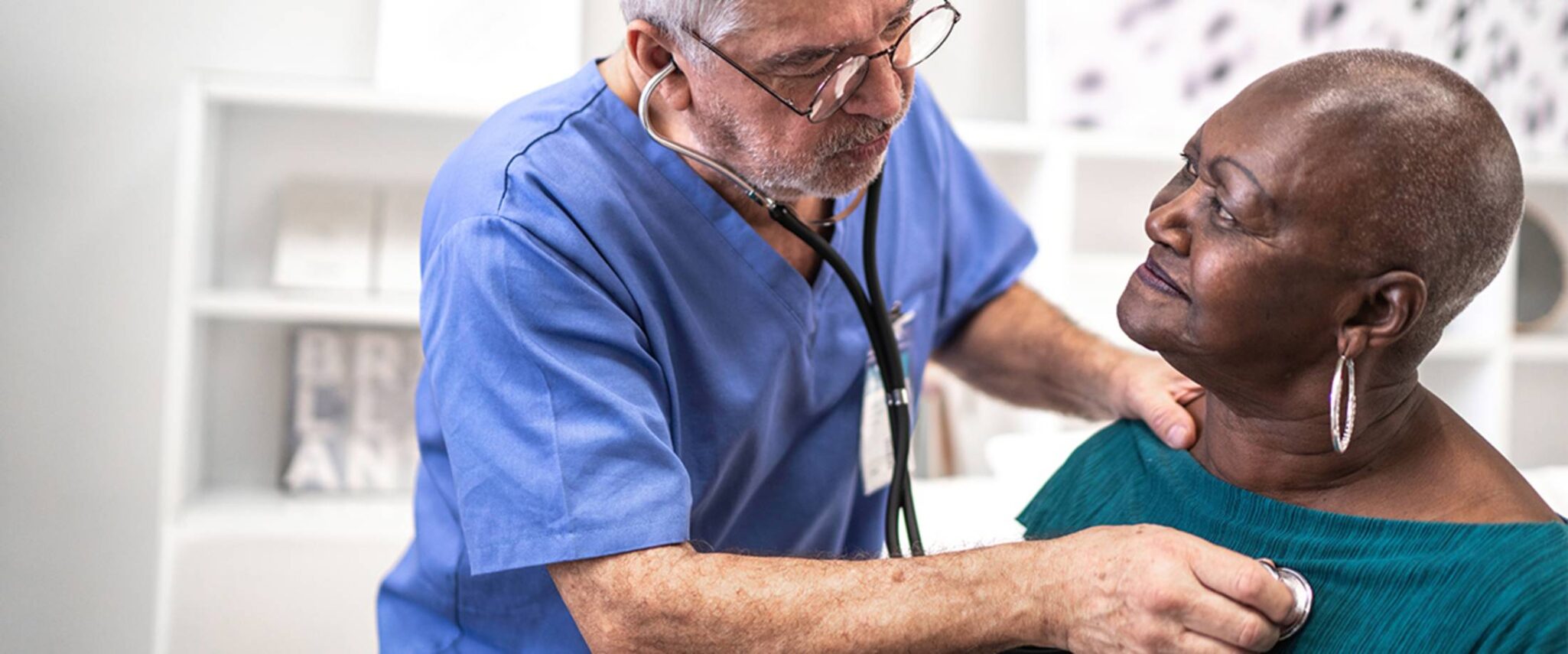 male nurse listening to a senior woman's heartbeat through a stethoscope