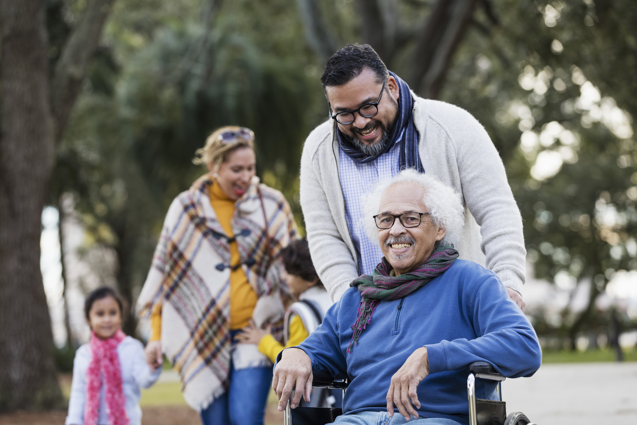 Smiling senior man in wheelchair at park with his adult son and family