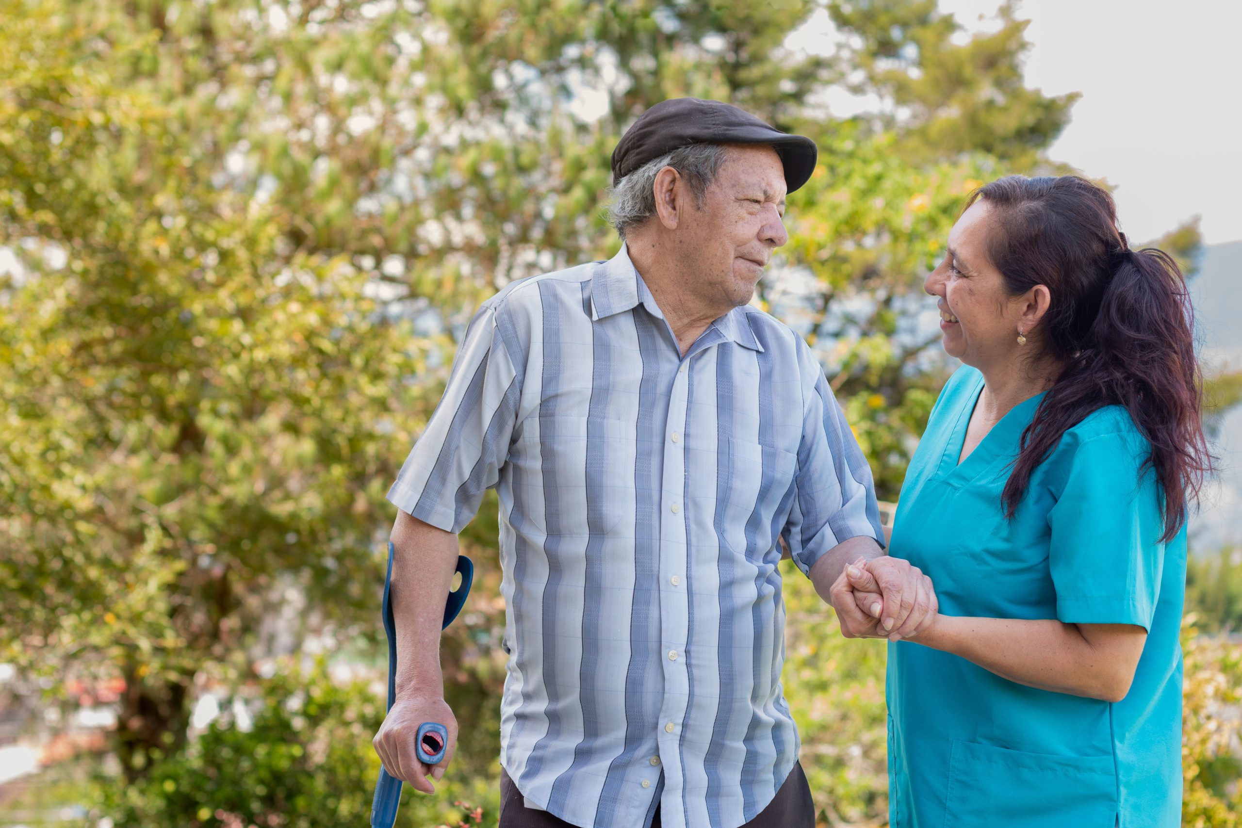 Senior man with cane holding hands with female nurse in park