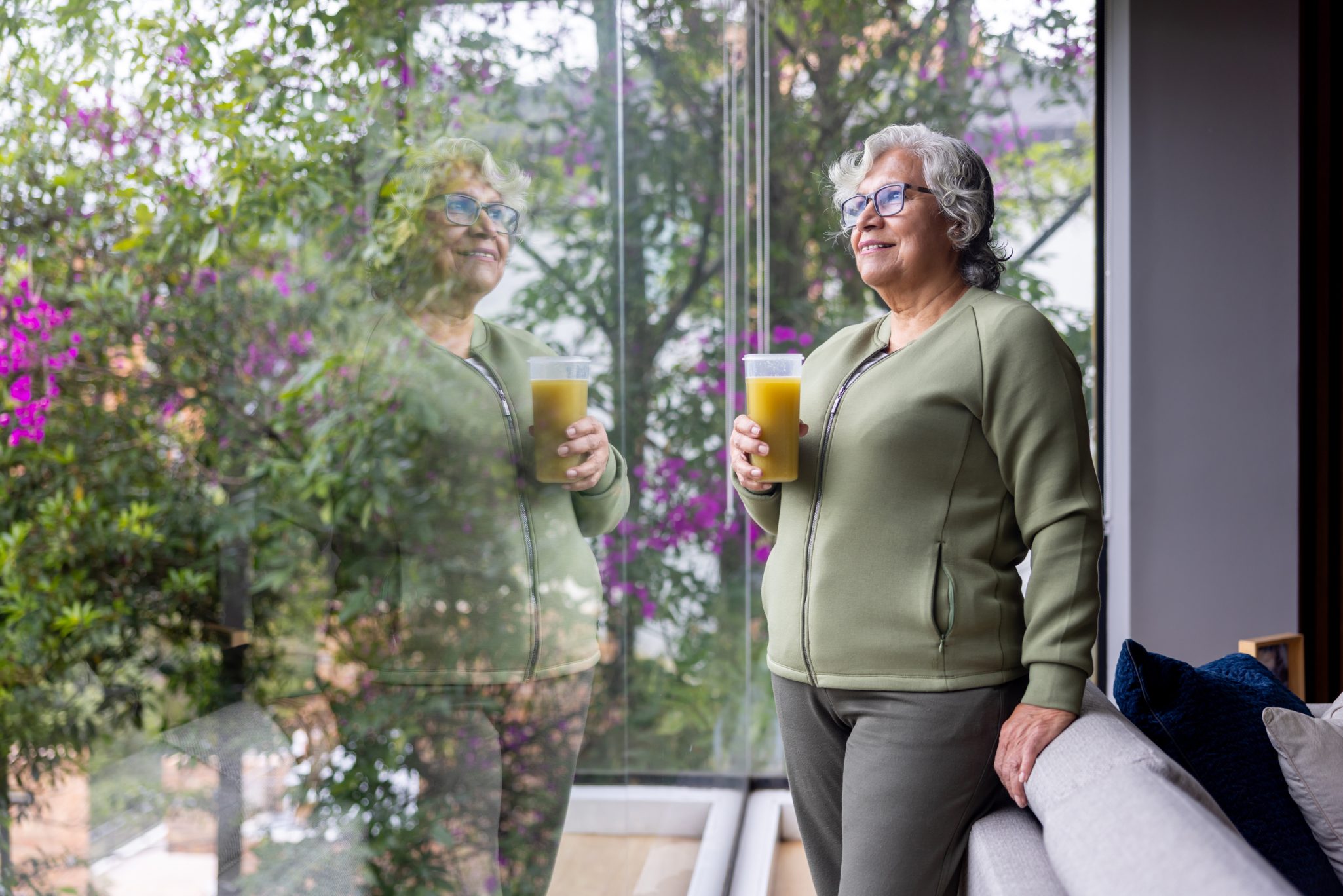 Senior woman holding smoothie while looking out window